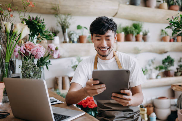 small business owner smiling while managing his website hosting services on a tablet in a flower shop